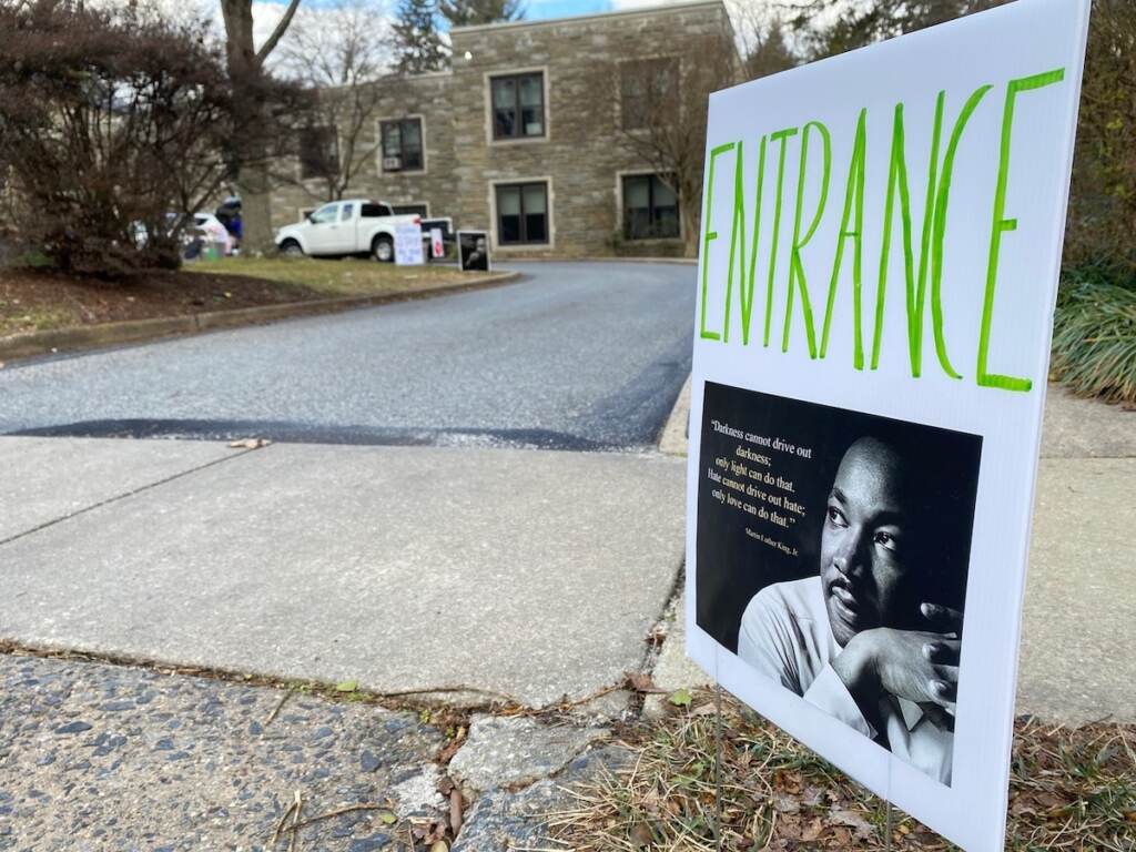 A sign with a photo of Dr. Martin Luther King Jr. and the word "entrance" is visible in the foreground. A parking lot and a building are visible in the background.