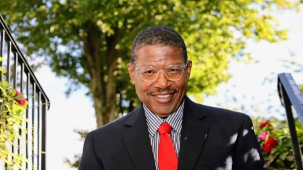 A man smiles for a photo. A tree is visible in the background.