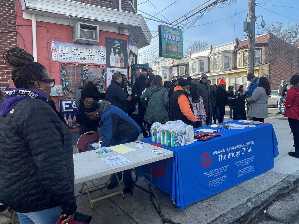 A group of people stand around a folding table on a street corner.