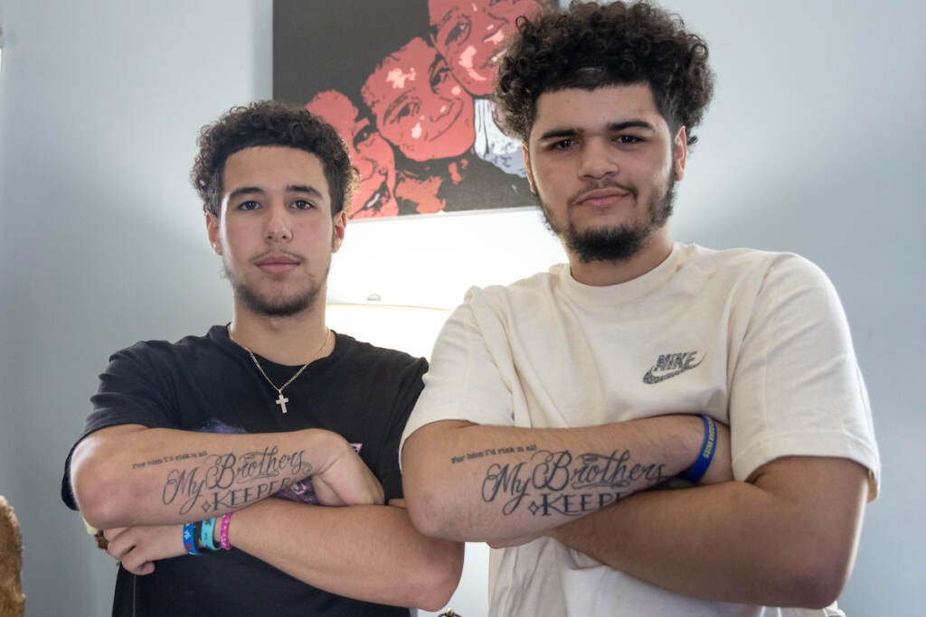 Two friends pose, arms crossed, showing their matching tattoos.
