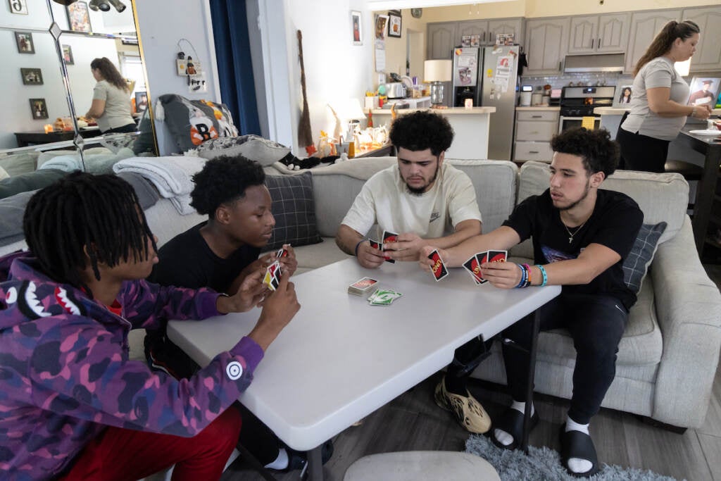 A group of teens play Uno at a table in the middle of a living room.