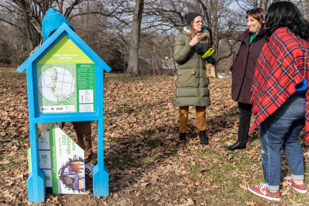 A group of people stand next to a sign in a grassy area.