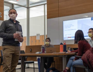 A person stands at the front of a room where students are seated.