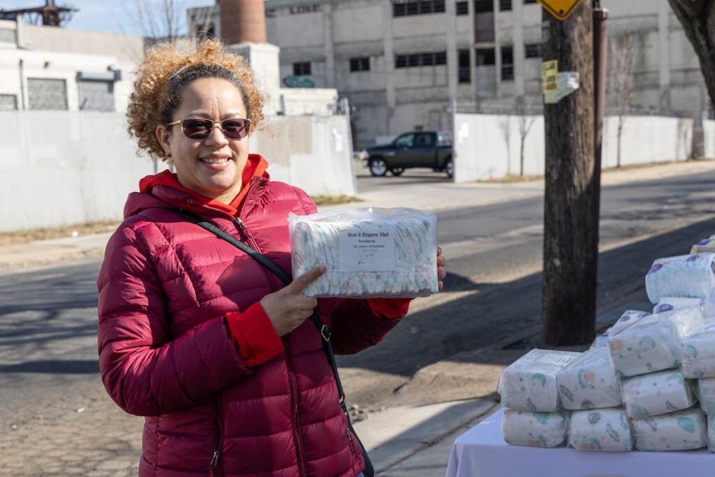 Emely Camilo holds up a package of diapers. Behind her is a street and some buildings.