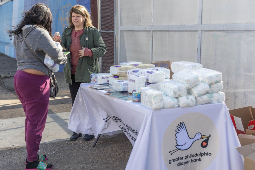 Two people stand by a table full of diapers and other supplies.