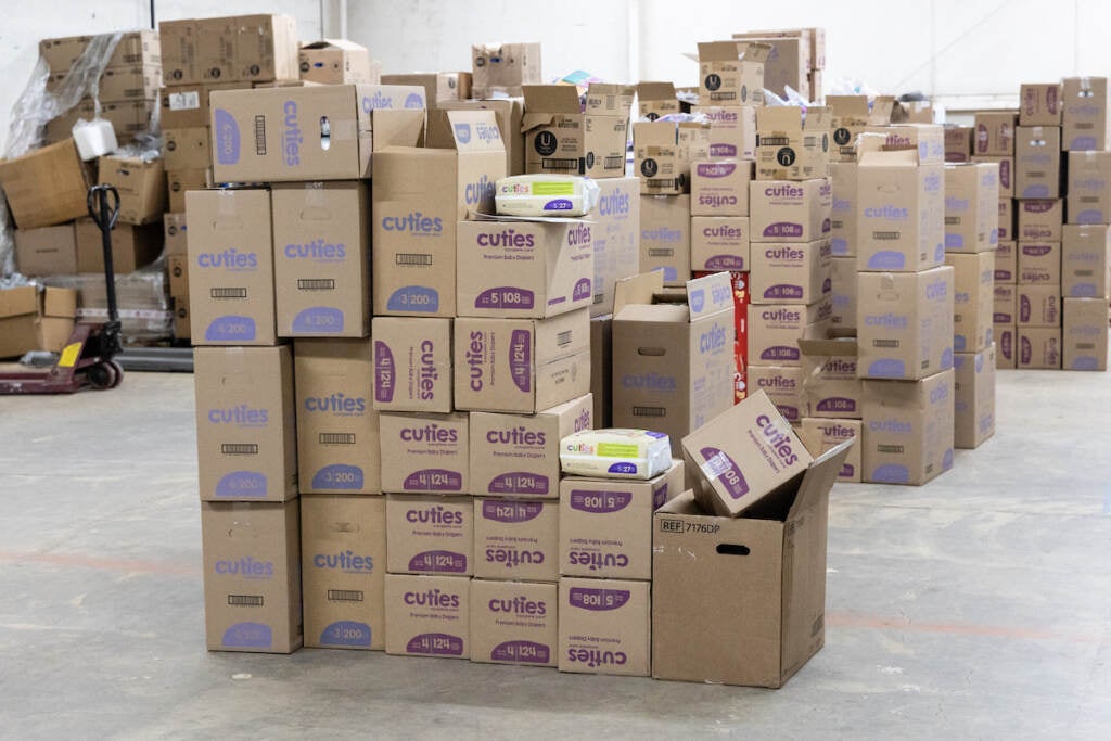 Cardboard boxes of diapers are visible in a warehouse.