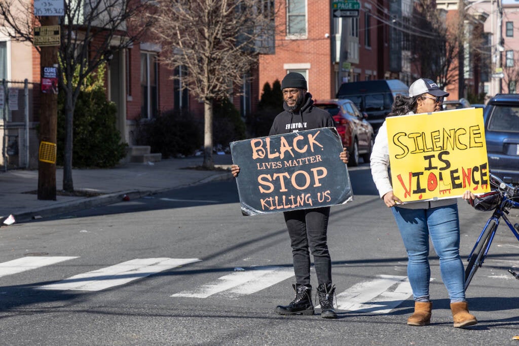 Protesters hold signs on a street corner.