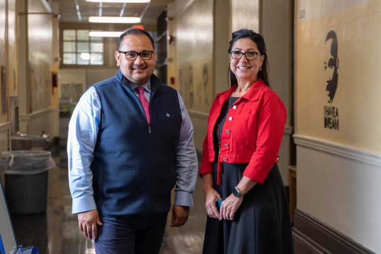 Two people smile as they pose in a school hallway.