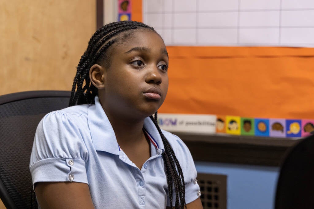 Zuri looks to the front of the classroom as she sits in a chair.