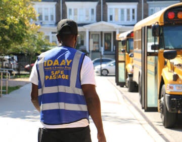 A person wearing a security vest walks near school buses.