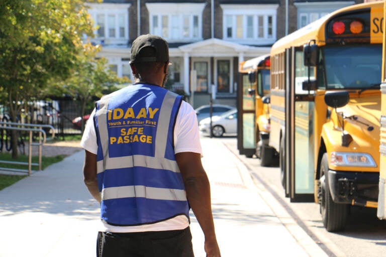 A person wearing a security vest walks near school buses.