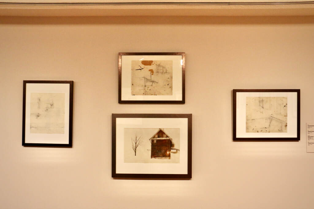 A series of paintings and drawings are framed and hung on a wall.