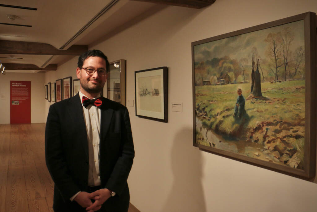 A person stands next to a painting hung on a wall.