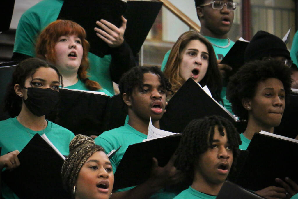 Students sing in a choir, wearing green T-shirts.