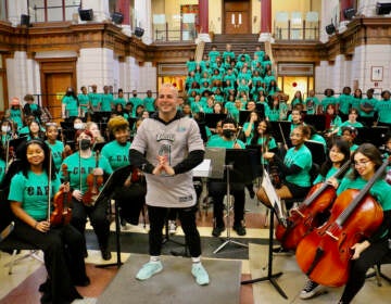 The conductor poses with a group of students in an orchestra.