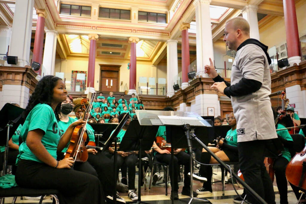 A conductor speaks with a student in the orchestra.