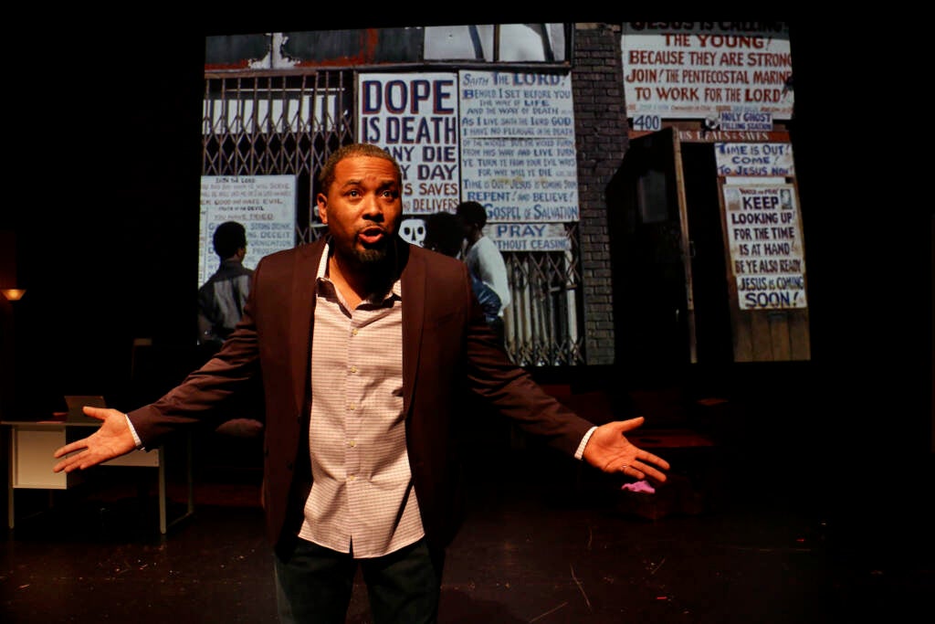 A man onstage gestures with his hands as he speaks.