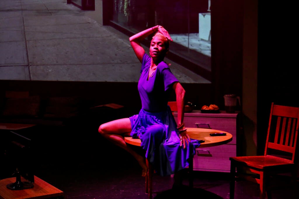 A woman dances on a table onstage during a production of "Mecca is Burning."