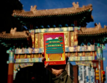 A book is held up in front of the ornate gateway in Philadelphia's Chinatown.