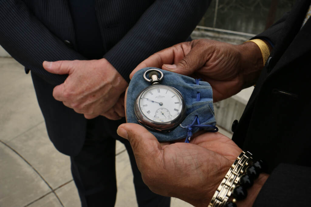 An up-close view of someone holding a pocket watch as another person looks on.