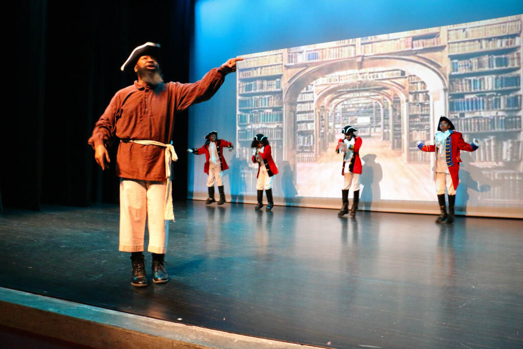 People in 18th-century clothing perform onstage.