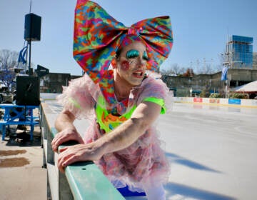 An ice skater and performer clutches the side of the ice skating rink on a sunny day.