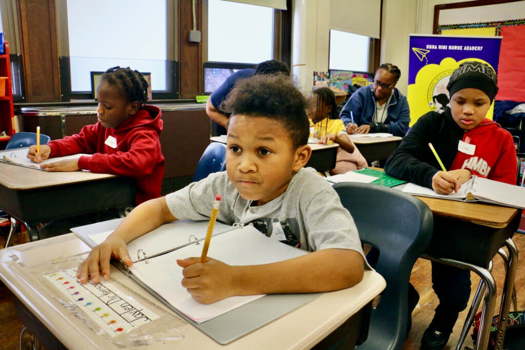 A students looks up, concentrated on the front of the room, as he writes something in his notebook.