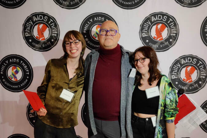 Michael Byrne (center), board president of Philly AIDS Thrift, gives a grant check to volunteers of Serenity House, Sydney Cox (left) and Ty Rizzo, during a ceremony at William Way Community Center on Spruce Street. (Peter Crimmins/WHYY)