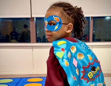 A girl poses with a superhero cape and mask.