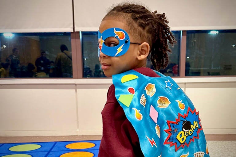 A girl poses with a superhero cape and mask.