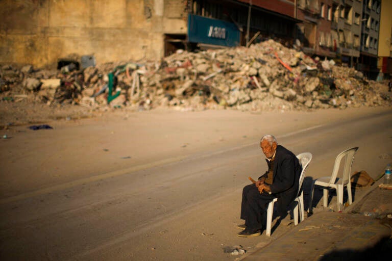A man sits on a chair next to rubble of a destroyed building in Iskenderun city, southern Turkey, Tuesday, Feb. 14, 2023. Thousands left homeless by a massive earthquake that struck Turkey and Syria a week ago packed into crowded tents or lined up in the streets for hot meals as the desperate search for survivors entered what was likely its last hours. (AP Photo/Francisco Seco)