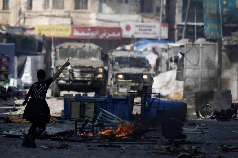 A Palestinian gestures to Israeli military vehicles during clashes in the West Bank city of Nablus