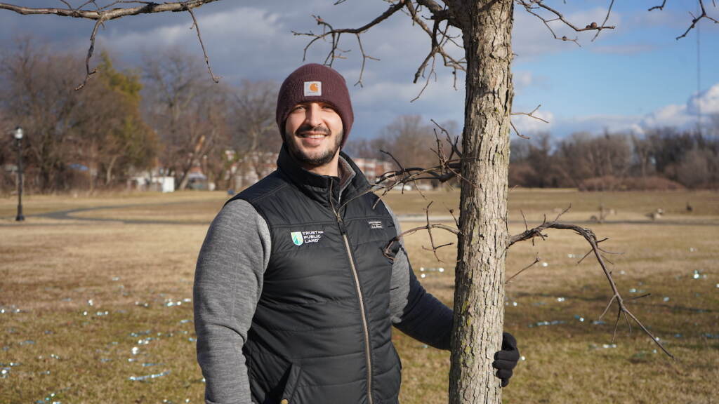 A man stands next to a tree in an open field.