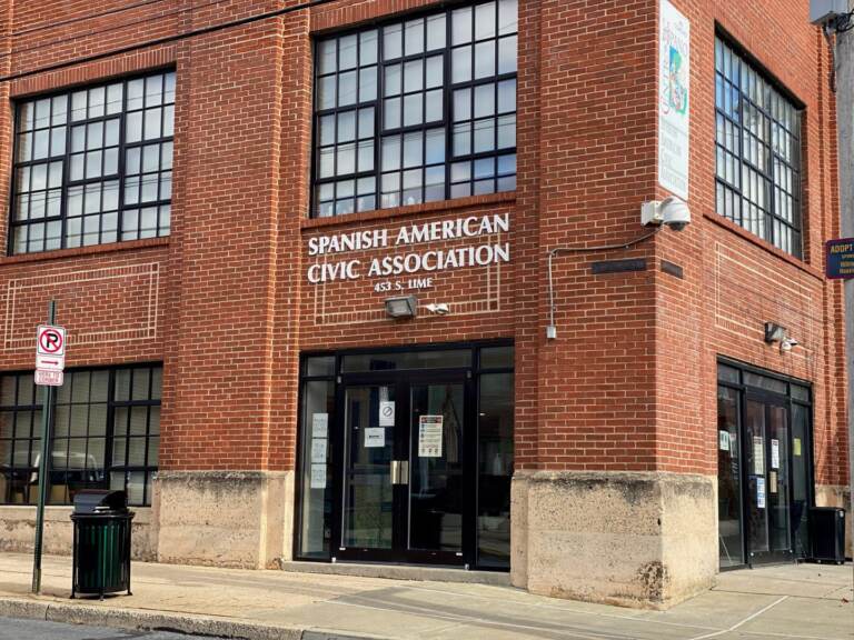 A view from the sidewalk of a red-brick building with a sign that reads Spanish American Civic Association.