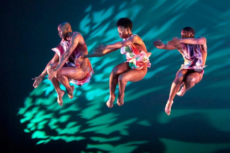 Dancers leap in the air against a colorful backdrop.