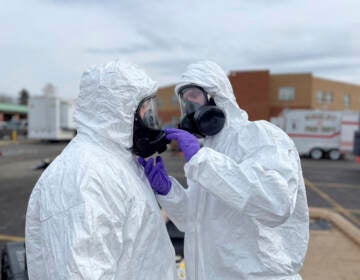 Two people in hazmats suits check each others' masks.