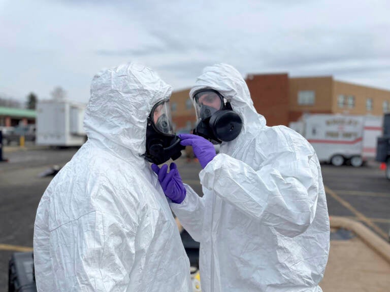 Two people in hazmats suits check each others' masks.