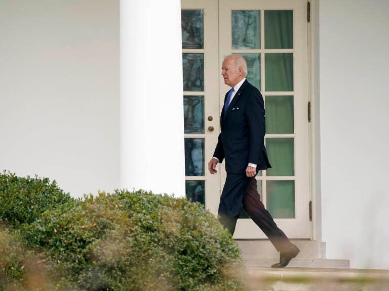 Biden walks in an outdoor corridor at the White House.