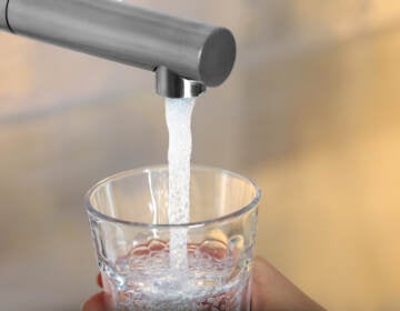 Woman filling glass with tap water from faucet on blurred background, closeup