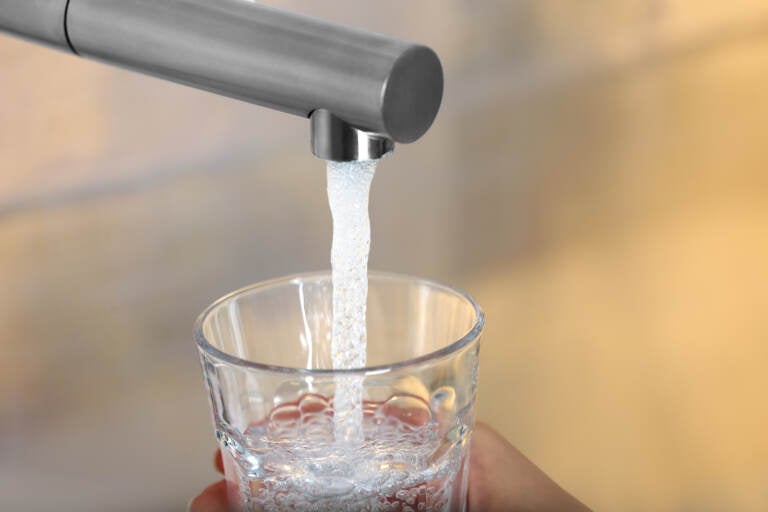 Woman filling glass with tap water from faucet on blurred background, closeup