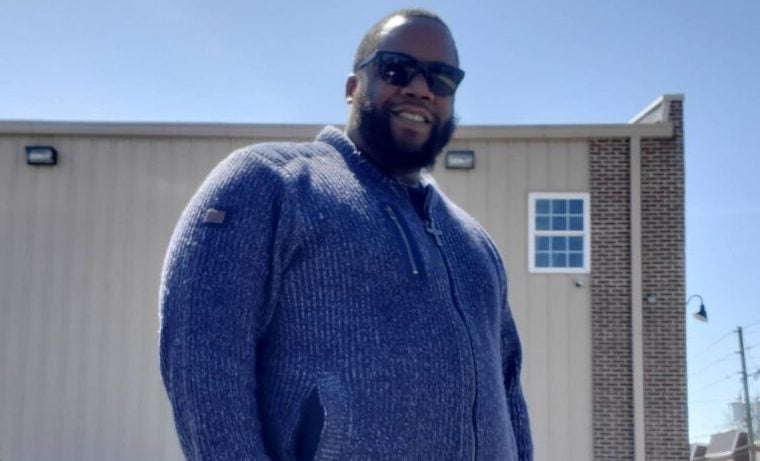 A man smiles outside of a building on a sunny day.