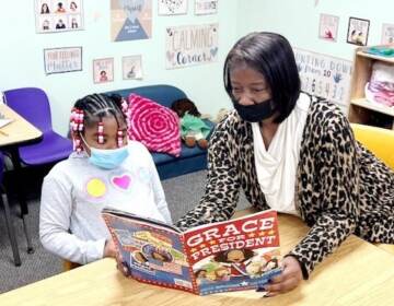 Melanie Price reads a book with a child in a classroom.