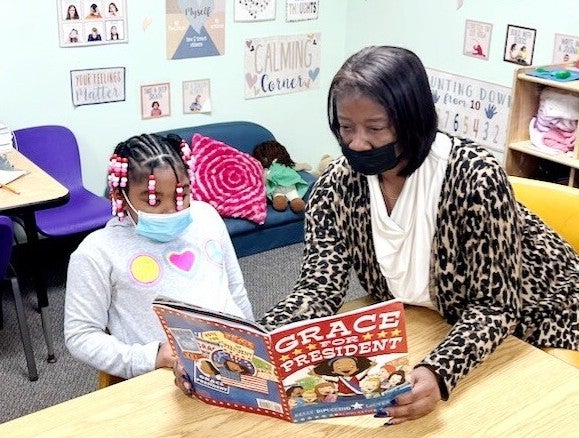 Melanie Price reads a book with a child in a classroom.