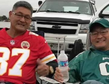 Two brothers wearing Chiefs and Eagles jerseys, respectively, pose for a photo.