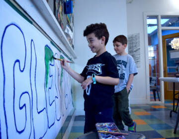 A kid paints a letter in a large sign that reads, 