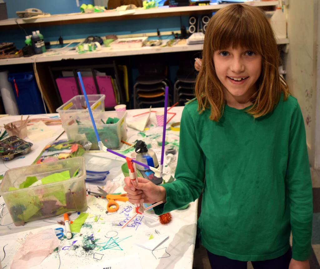 A child holds a field gold post she made with straws.