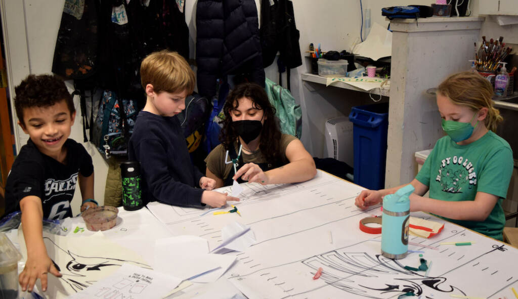 A teacher and students sit around at able doing crafts.