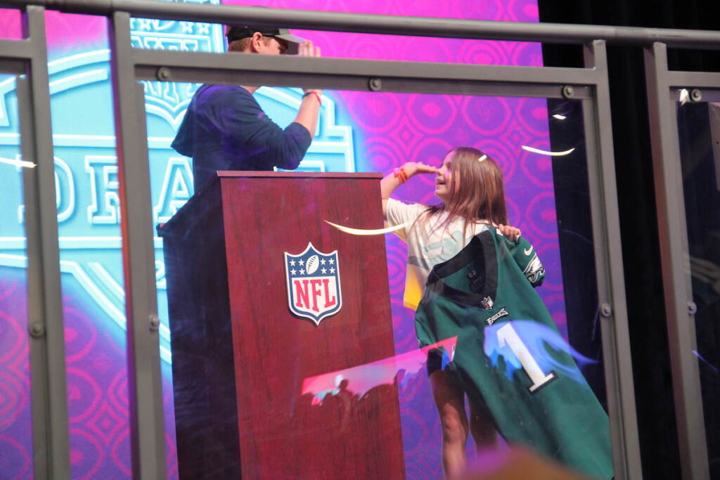 A little girl holding an Eagles jersey high-fives someone at a podium.