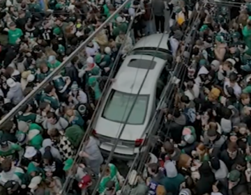 An aerial view of a silver car surrounded by a large crowd of people wearing green.