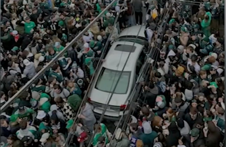 An aerial view of a silver car surrounded by a large crowd of people wearing green.